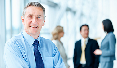 A photo of a businessman posing in front of 3 colleagues discussing a previous meeting.